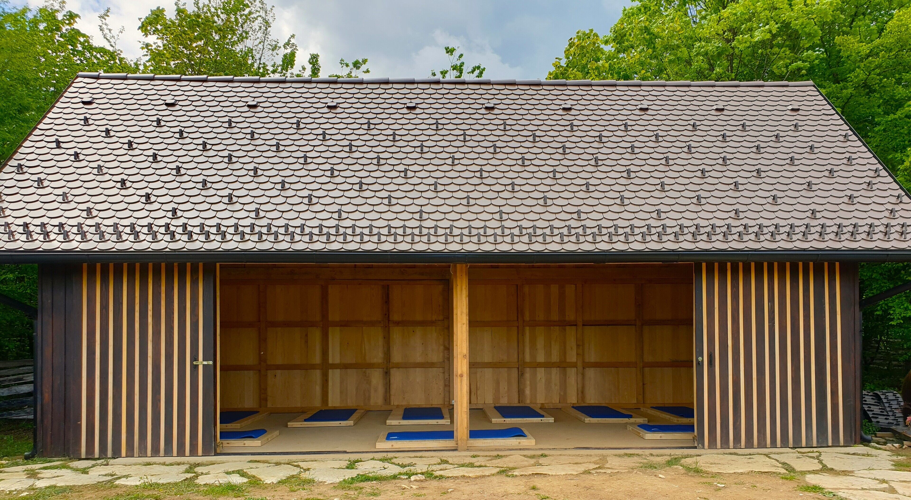 A building with a tiled roof and a large open wooden interior with blue mats on the floor.