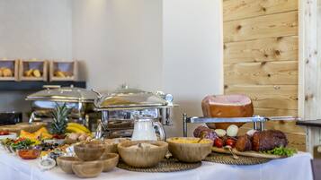 Una mesa de buffet con diversos alimentos, como frutas, verduras y carnes, en una sala con paredes de madera y un mantel blanco.