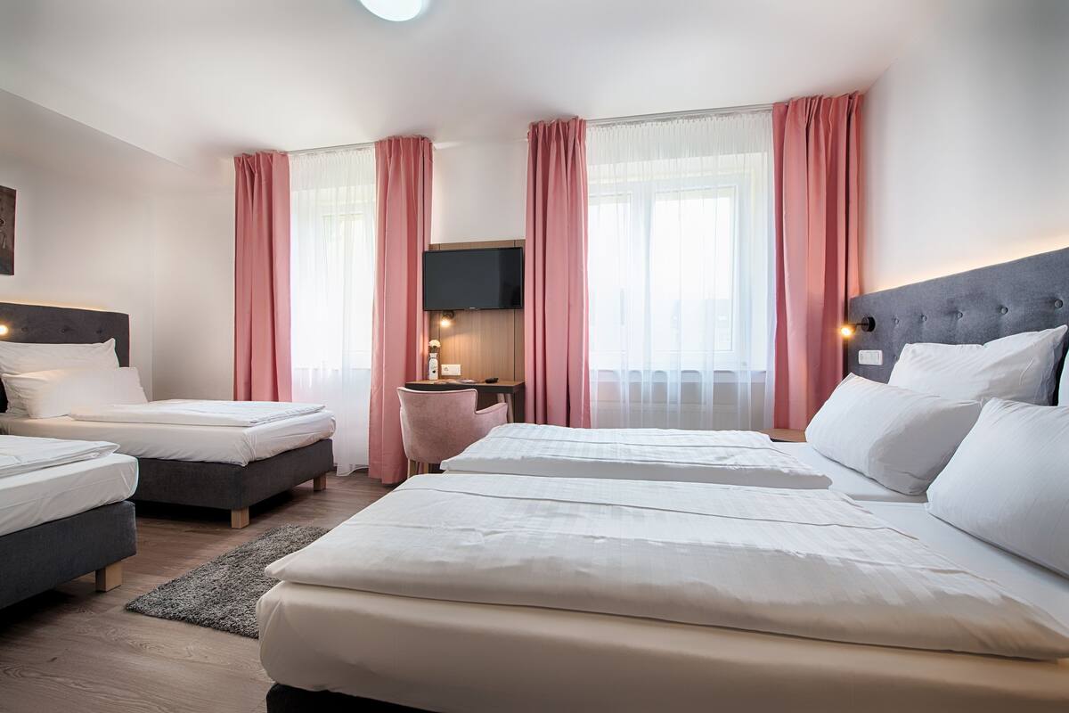 A hotel room with two beds, a desk, a TV, and pink curtains.