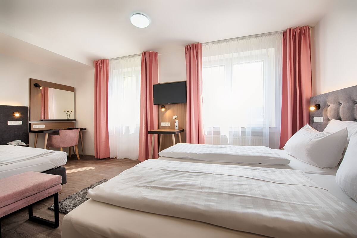 A hotel room with two beds, a desk, a chair, a TV, and a bathroom.