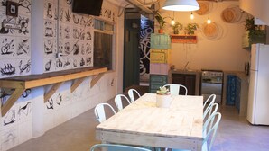A dining area with a wooden table and chairs, a wall with various drawings, and a kitchen area with appliances.