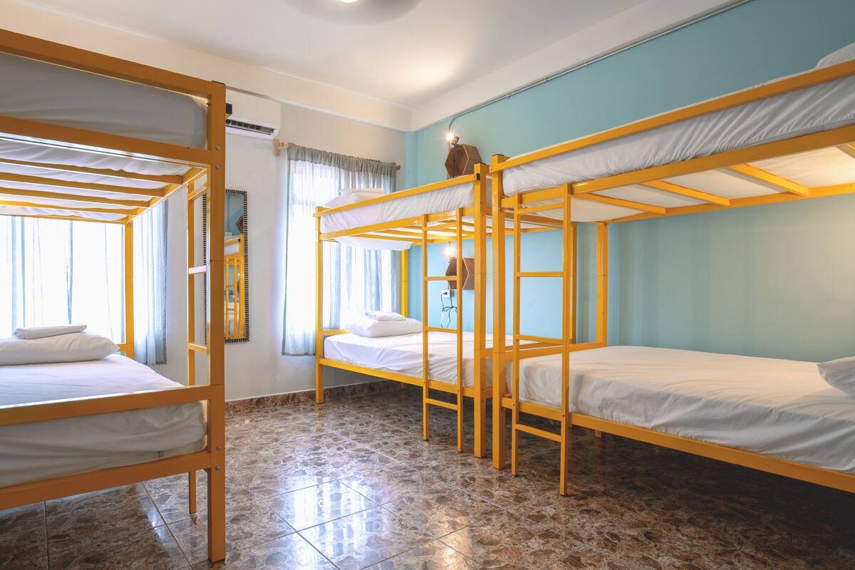Een studentenkamer met stapelbedden, een spiegel en een raam met gordijnen.