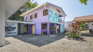 A two-story building with a purple and white facade, a covered outdoor seating area, and a mural on the side.