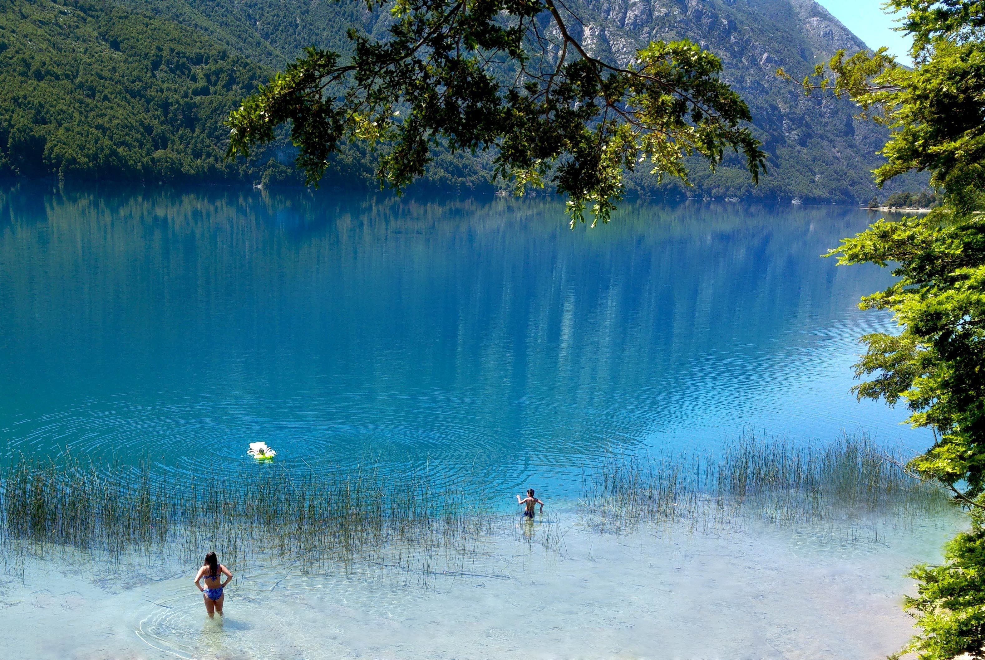 A clear lake with a boat and people in the water.