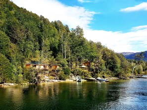 A lakeside cabin with a dock, surrounded by dense forest and mountains in the background. - Alma Patagonia Lodge (Futaleufú)