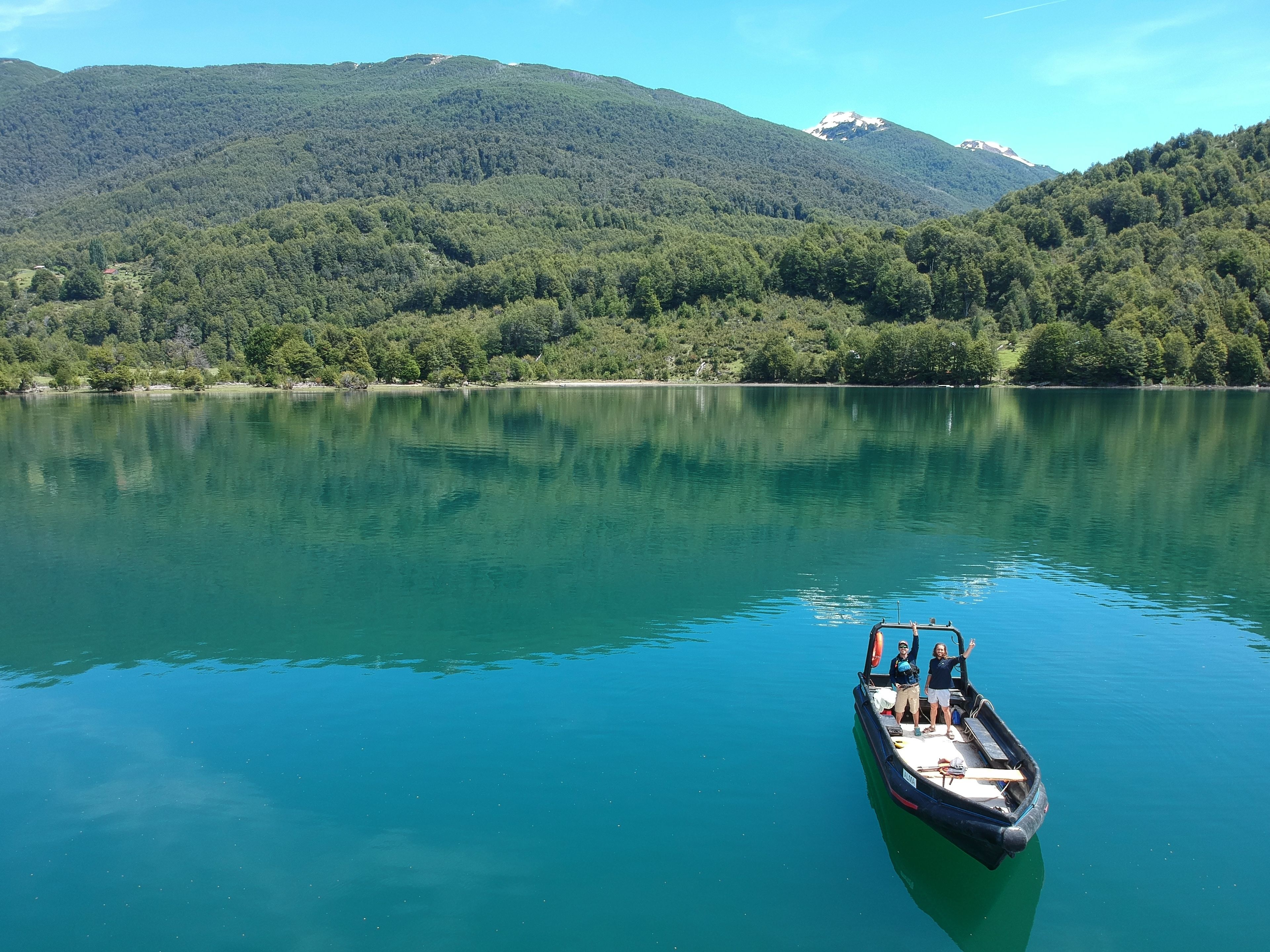A boat on a calm lake with a forested mountain in the background.
