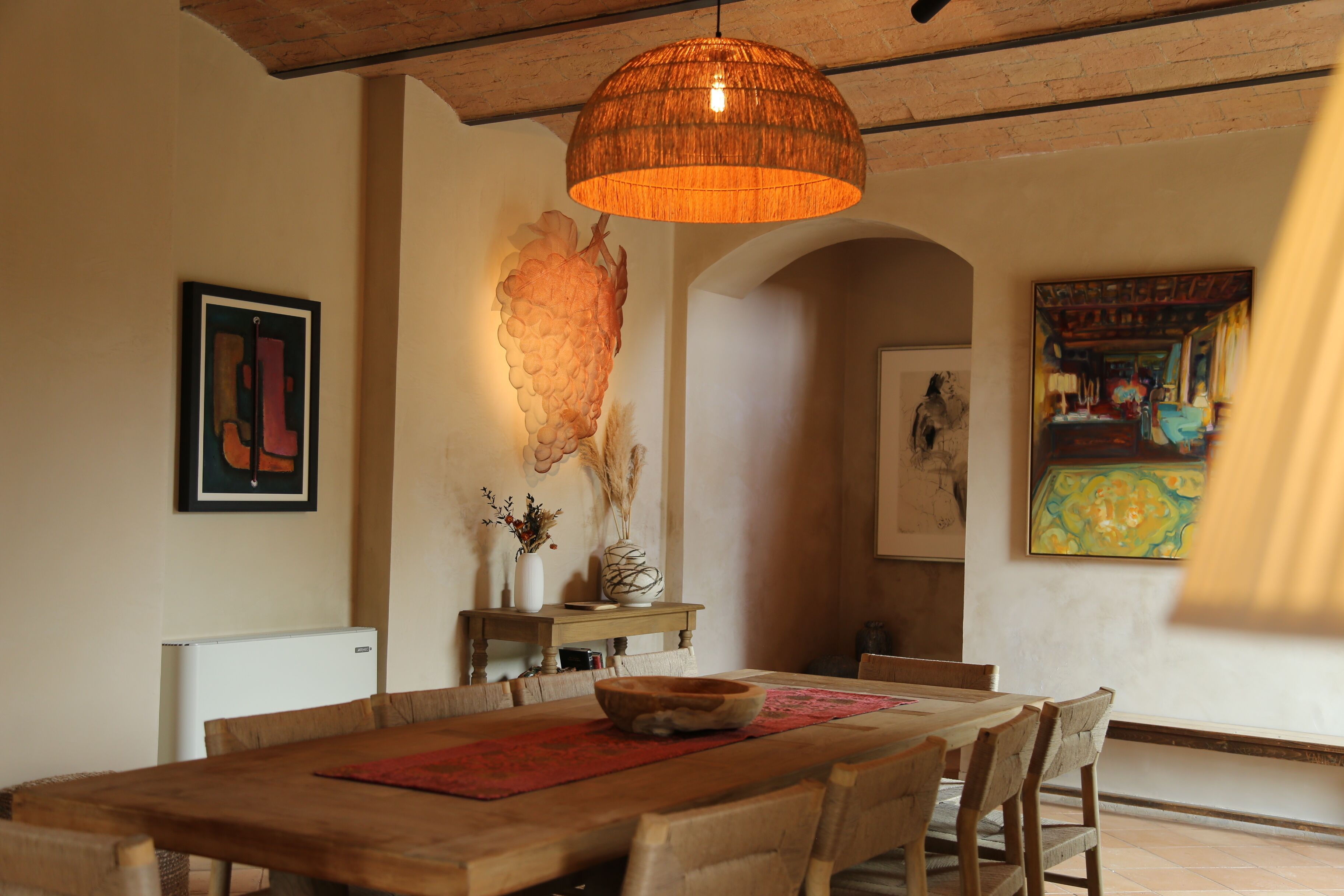 A dining area with a wooden table, chairs, a hanging orange pendant light, and artwork on the walls.
