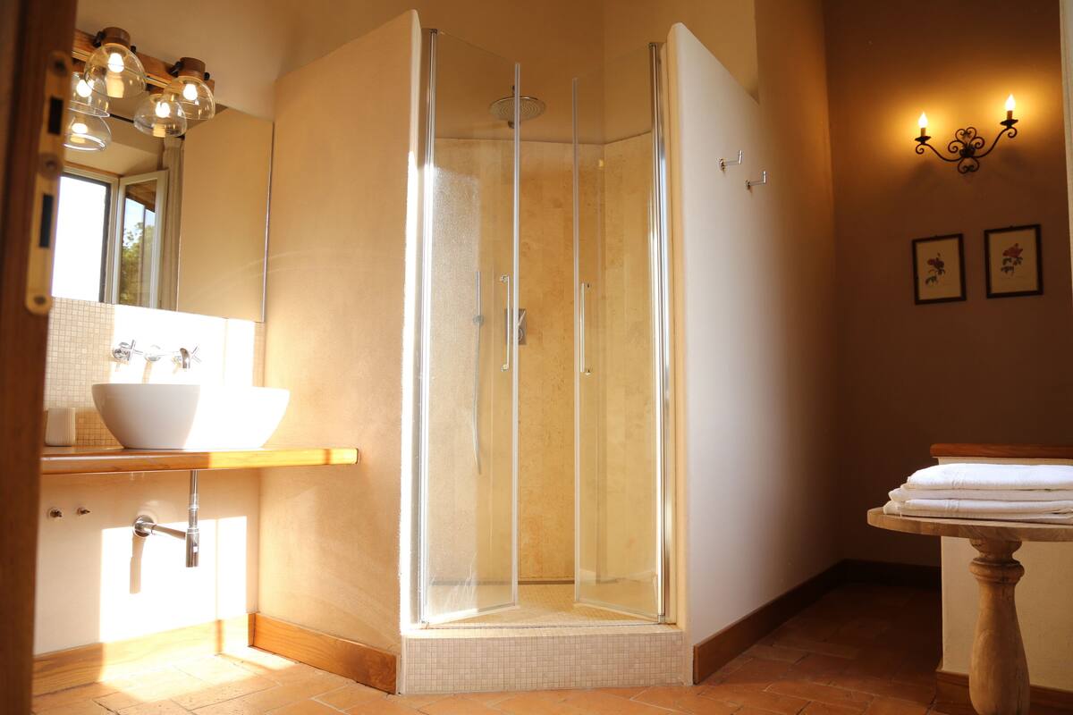 Een badkamer met een douche met glazen wanden, een witte wastafel en een houten opbergmeubel.