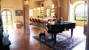 Een ruime kamer met een vleugelpiano, een bar en een groot raam met uitzicht op het landschap.