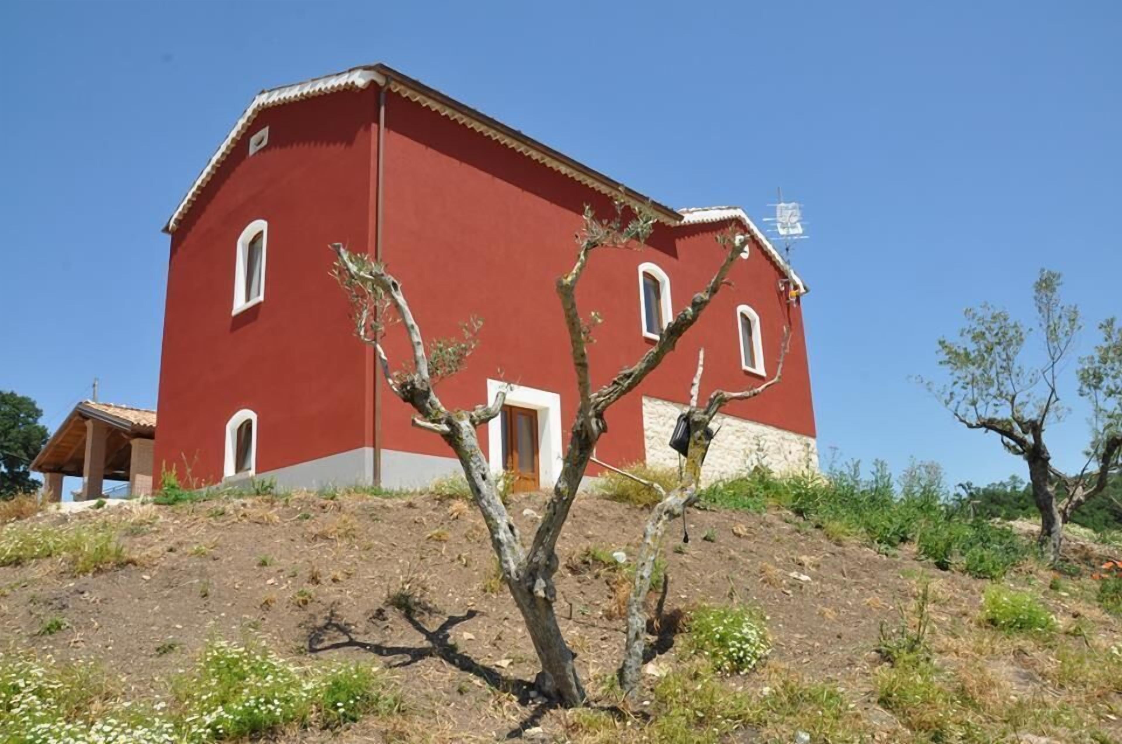 Ein rotes Gebäude mit mehreren Fenstern und einer Tür, umgeben von trockenem Gras und einigen Bäumen.