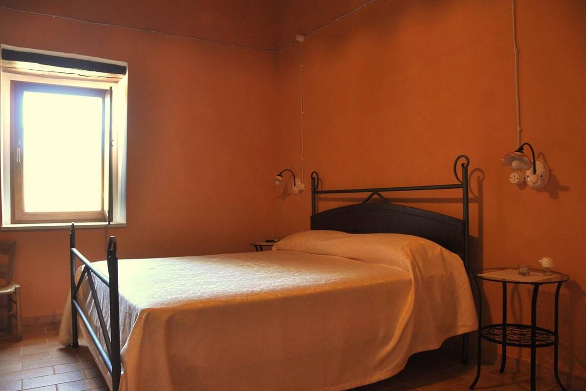 A single bed with a headboard, a small bedside table, a lamp, and a window with curtains.