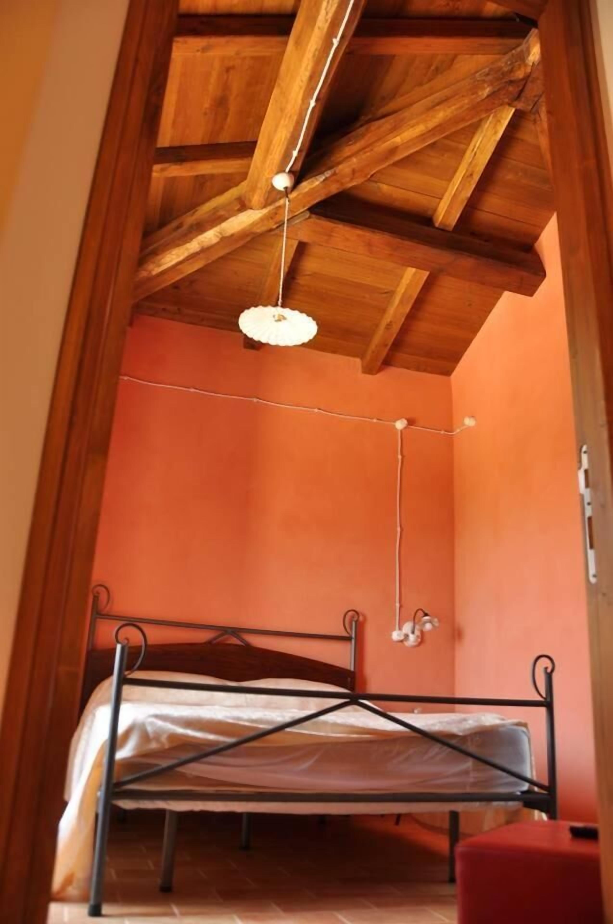 A narrow room with a single bed, wooden ceiling beams, and a hanging light fixture.