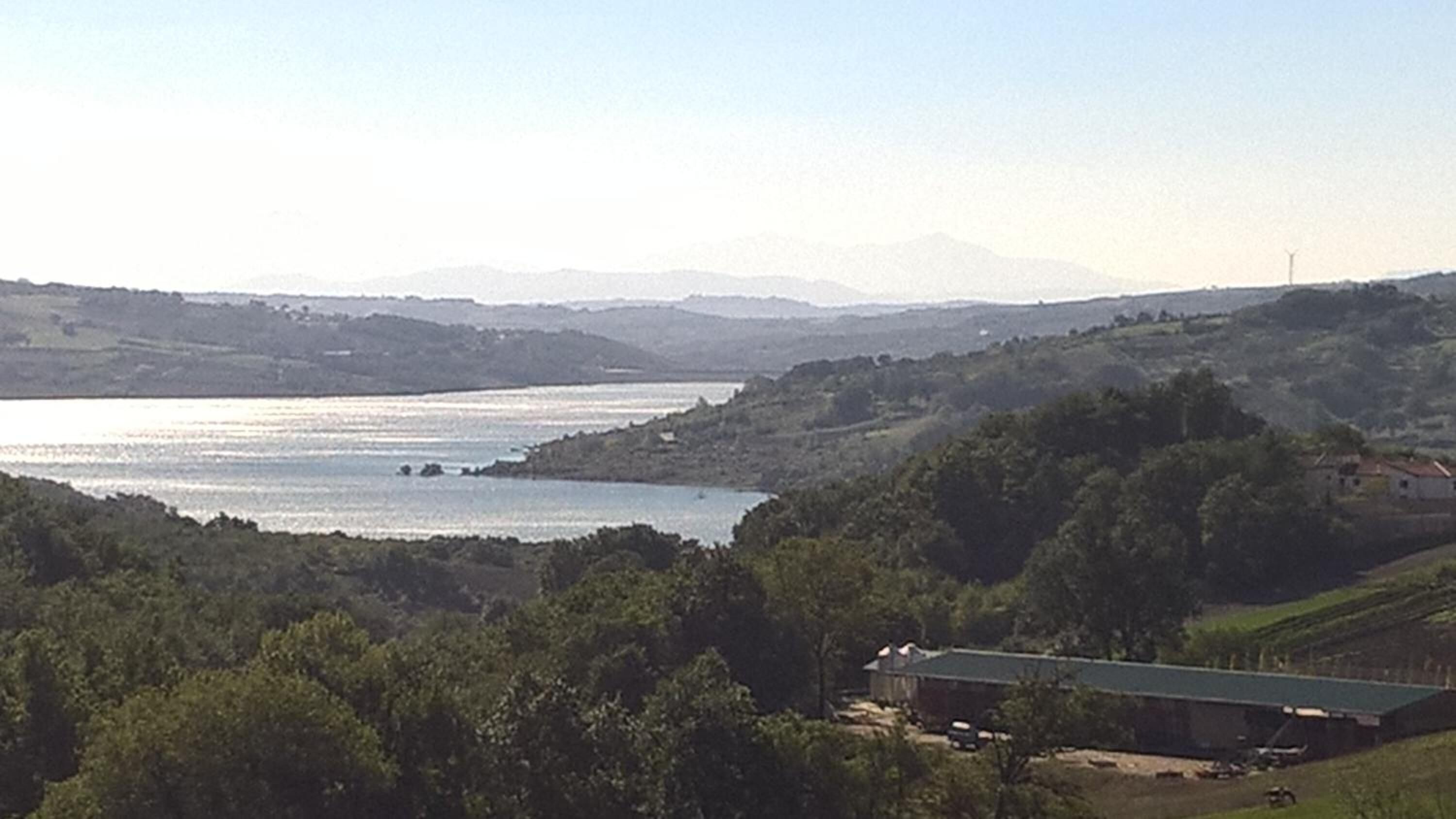 A view of a lake surrounded by hills and trees. There is a building with a green roof in the foreground.