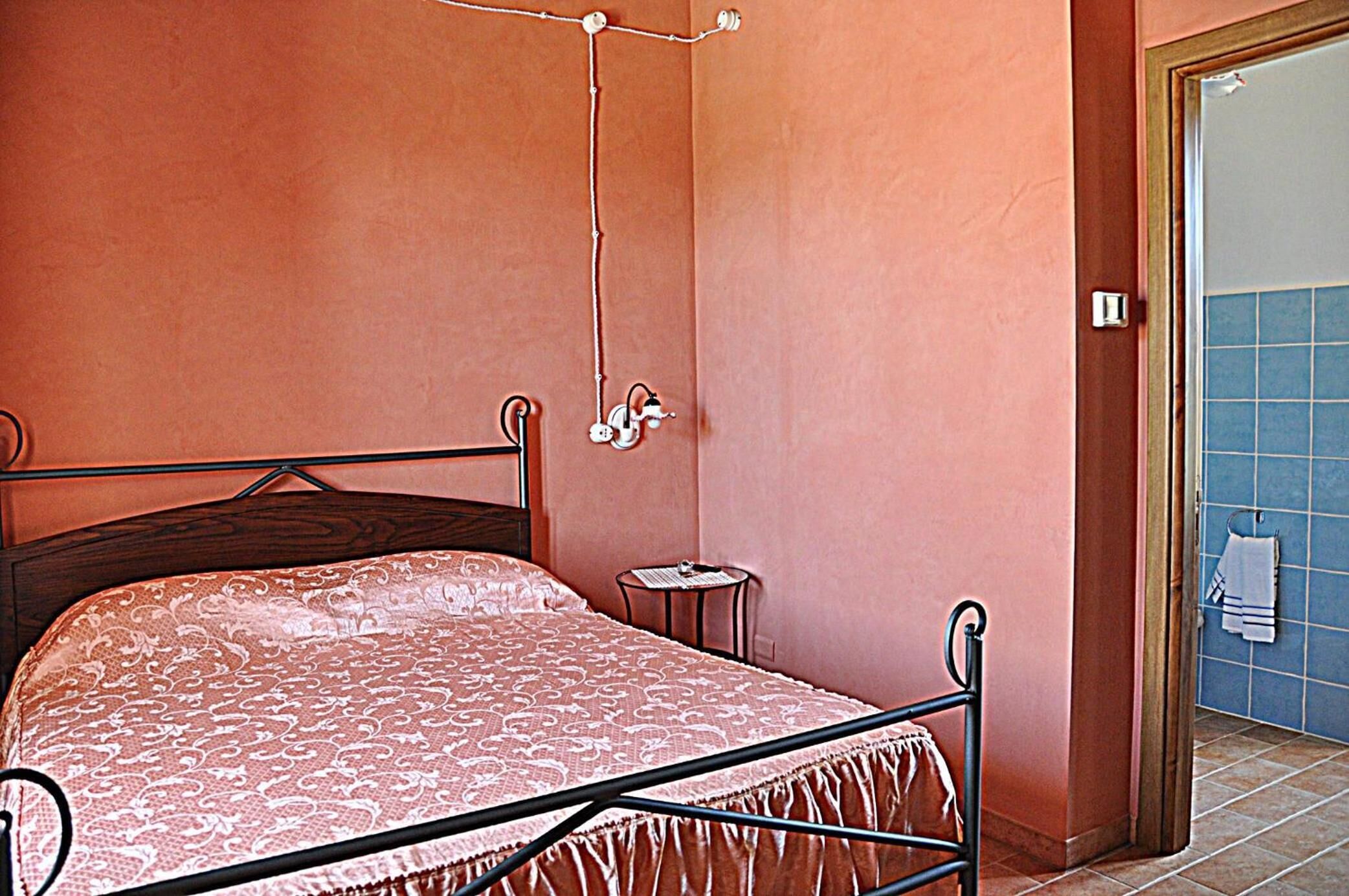 A bedroom with a bed, a small bedside table, and a door leading to a bathroom with blue tiles.