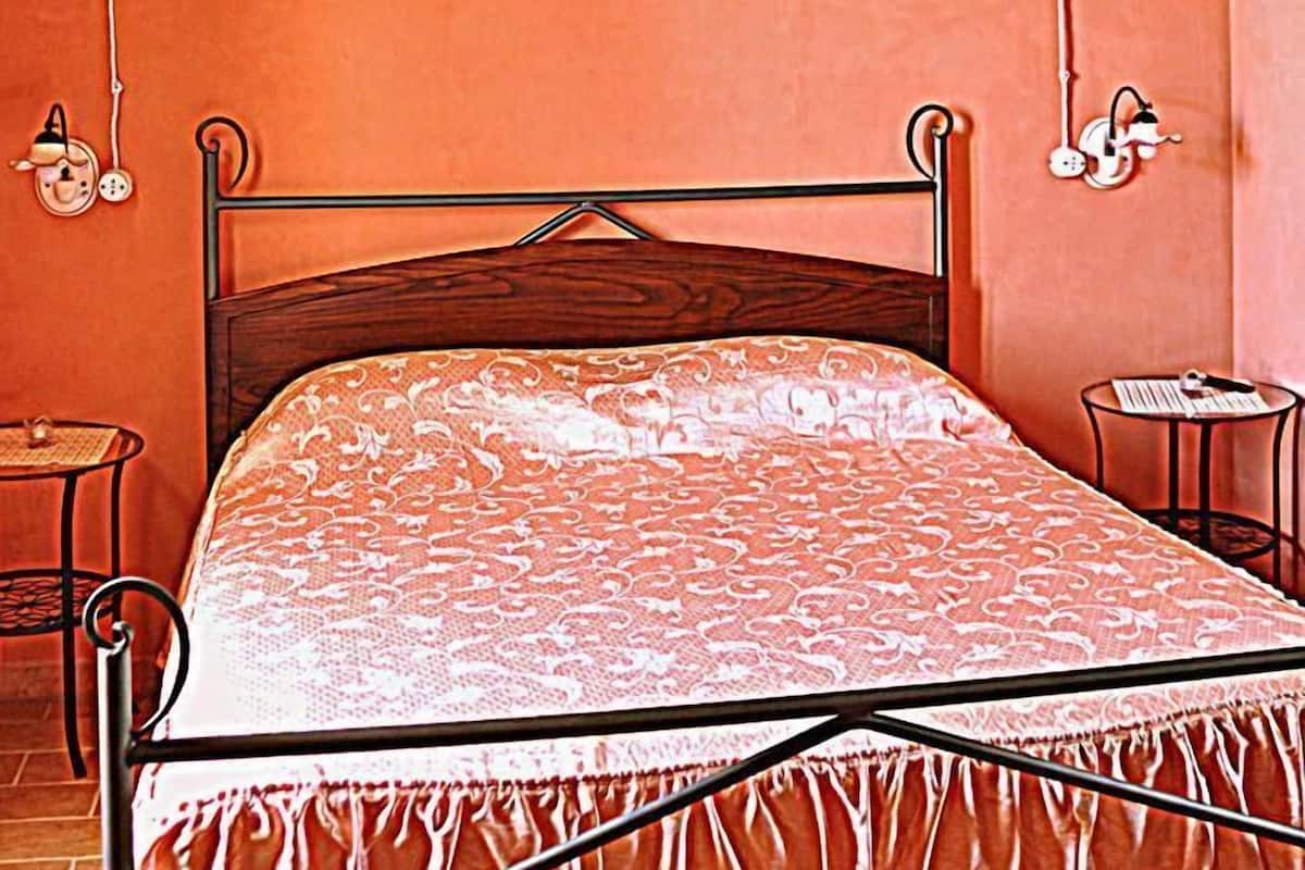 A bedroom with a wooden ceiling, a bed with a patterned bedspread, a bedside table, and a hanging light fixture.
