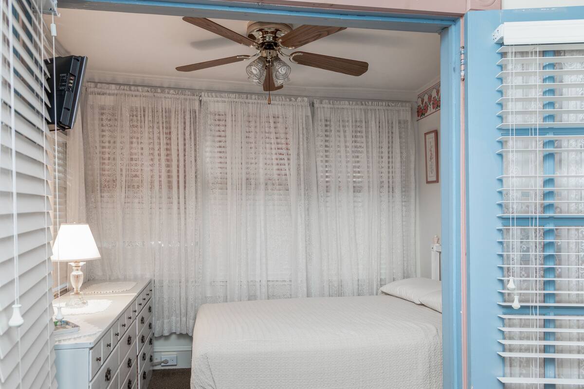 A bedroom with a bed, a ceiling fan, a nightstand with a lamp, and a dresser.