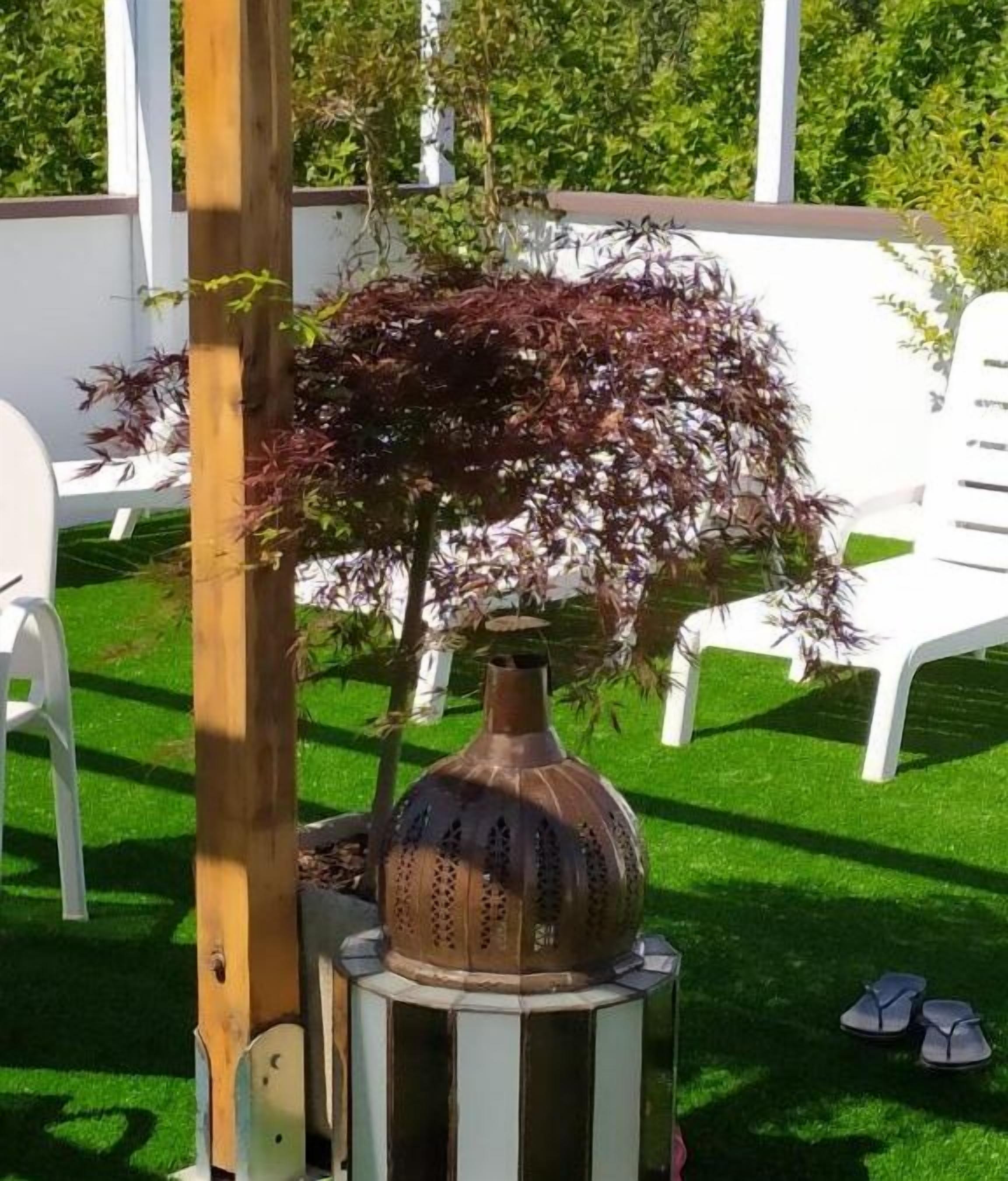Un espace patio agrémenté d’un vase en métal décoratif, d’un poteau en bois et d’une plante en pot aux feuilles rouges.