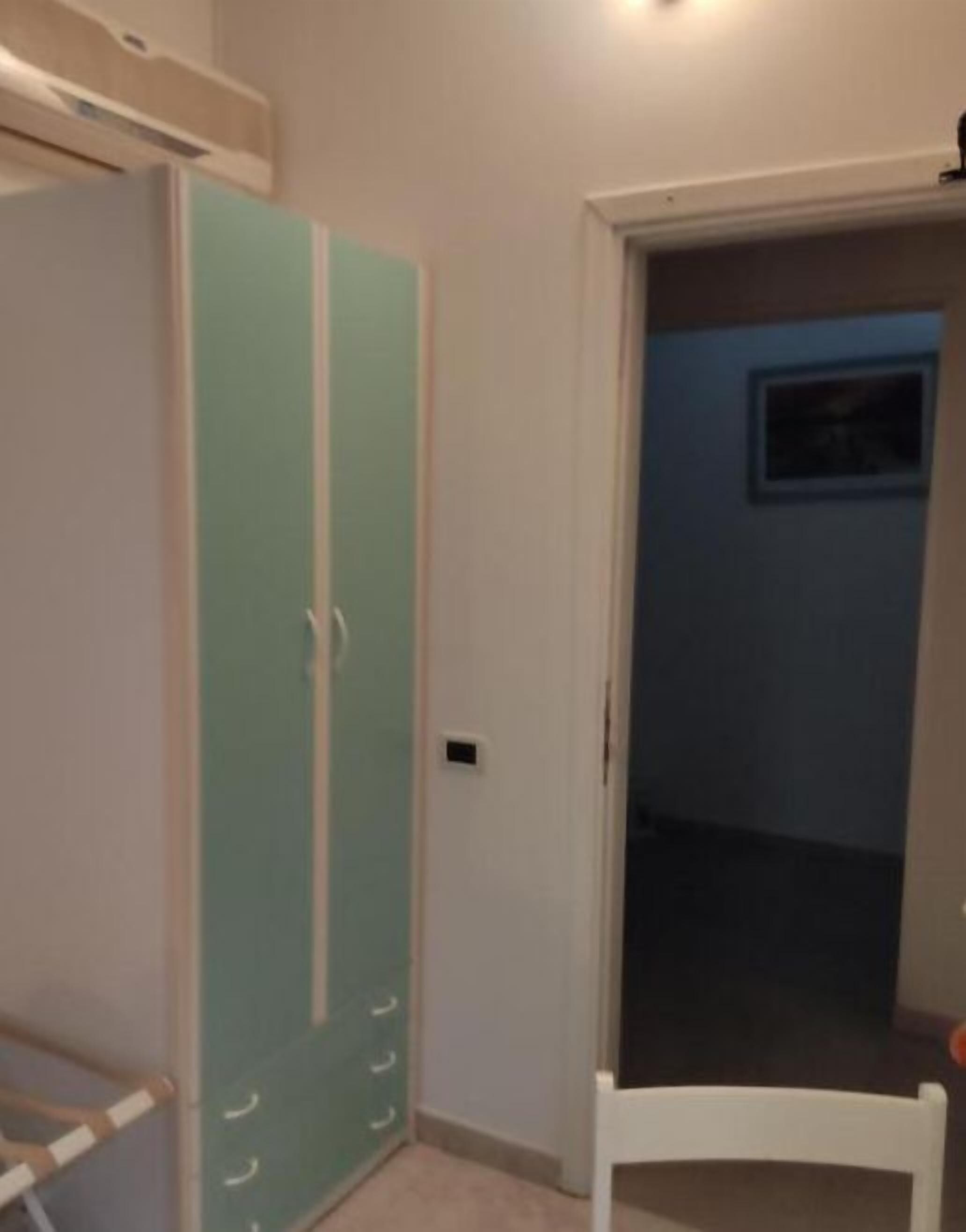 Una stanza con un armadio verde acqua, una sedia bianca e una porta che dà su un'altra stanza.