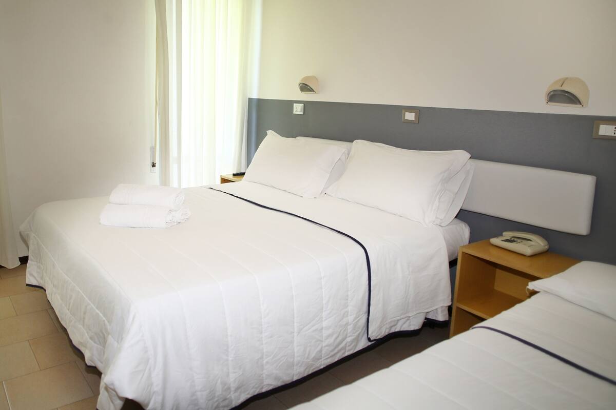 A hotel room with a large bed, bedside tables, a nightstand, and a window with curtains.