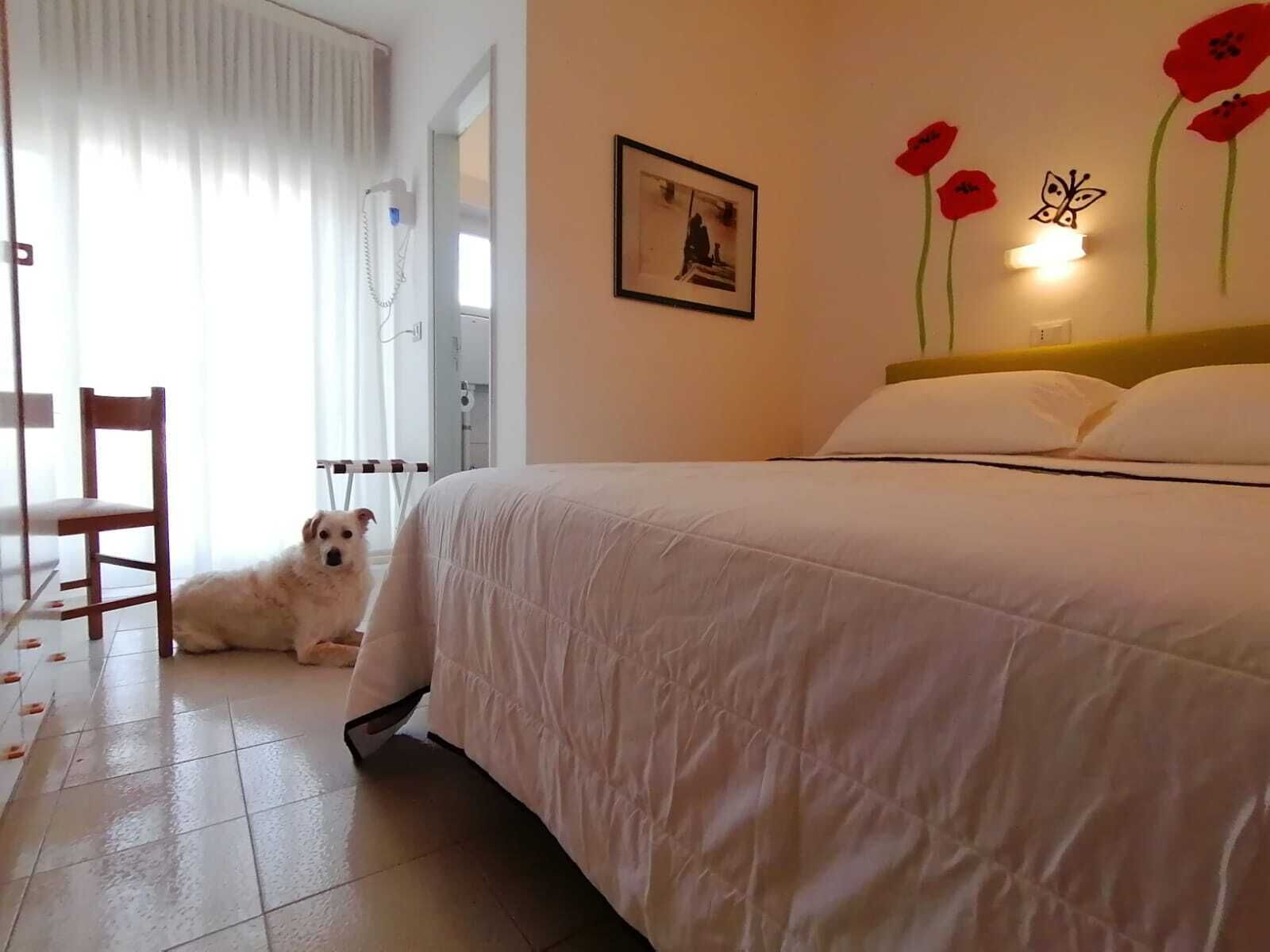 A bedroom with a bed, a chair, a dog, and a wall with a picture and flower decorations.