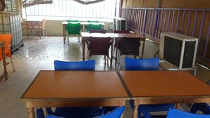 A classroom with wooden desks and blue chairs, a window with barred glass, and a tiled floor. - Hôtel Ma Résidence (Abidjan)