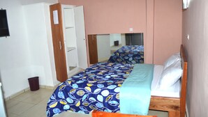 A bedroom with a bed, a mirror, a wardrobe, and a trash bin. - Hôtel Ma Résidence (Abidjan)