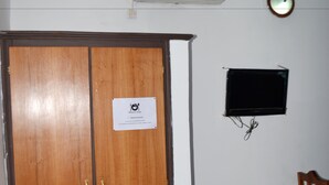 A room with a wooden wardrobe, a mounted air conditioner, a wall-mounted TV, and a small trash bin. - Hôtel Ma Résidence (Abidjan)