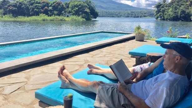 Un área junto a la piscina con sillas de descanso y vistas a un lago y montañas.