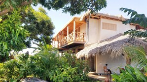 Un jardín tropical con una terraza de madera y una estructura cubierta de paja.