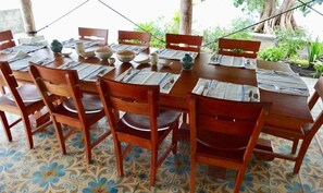 Una mesa de madera para comer con platos, cuencos y cubiertos, rodeada de sillas.