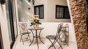 A small patio area with two metal chairs and a round table, a vase with flowers, and a brick wall. - Heliko 101A by CocoBR (Playa del Carmen)