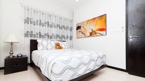 A bedroom with a bed, a nightstand, a lamp, a teddy bear, a painting, and a door. - Heliko 101A by CocoBR (Playa del Carmen)