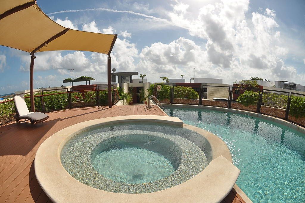 A hot tub surrounded by a wooden deck, with lounge chairs and a canopy.
