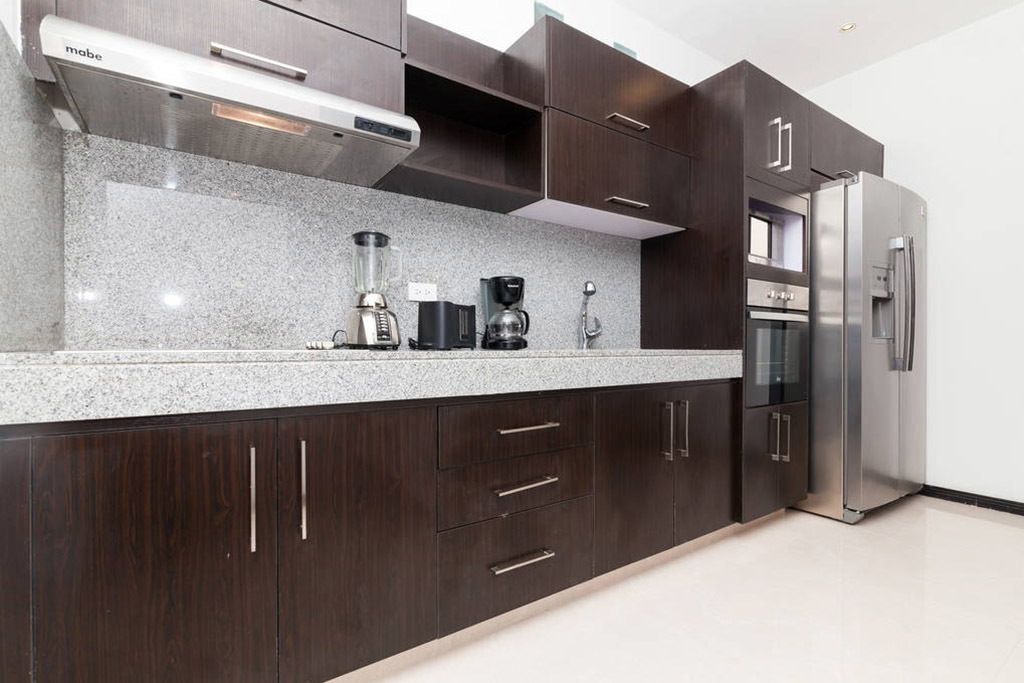 Una cocina moderna con armarios de madera oscura, un refrigerador de acero inoxidable, horno empotrado y cafetera.