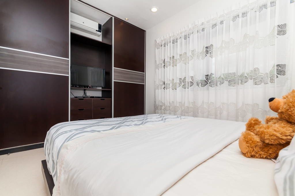 A bedroom with a bed, a television on a stand, a wardrobe, and a teddy bear on the bed.