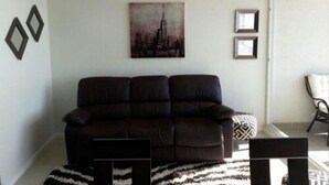 Ein Wohnzimmer mit einem dunkelbraunen Sofa, einem gemusterten Teppich und einem Stadtbild an der Wand.