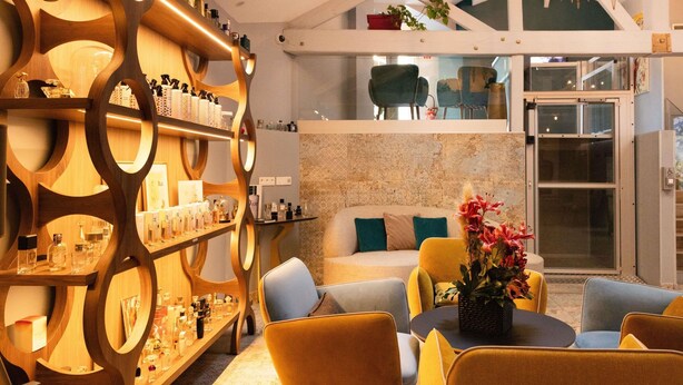 A modern interior with a wooden shelving unit displaying various bottles, a seating area with yellow chairs, and a stone wall. - Hôtel Mercure Paris Suresnes Longchamp (Suresnes)
