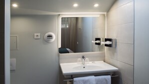 A modern bathroom with a white sink, mirror, and towel rack. There are ceiling lights and a window above the mirror. - Hôtel Mercure Paris Suresnes Longchamp (Suresnes)