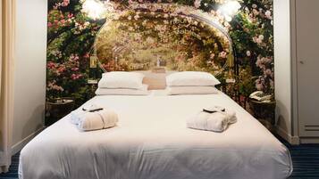 Habitación de hotel con una cama grande, dos mesitas de noche y un mural floral en la pared.