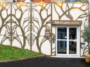 Exterior do Hotel Mercure, com design de fachada que lembra uma árvore, e uma placa indicando sua localização em Paris, Suresnes, Longchamp.