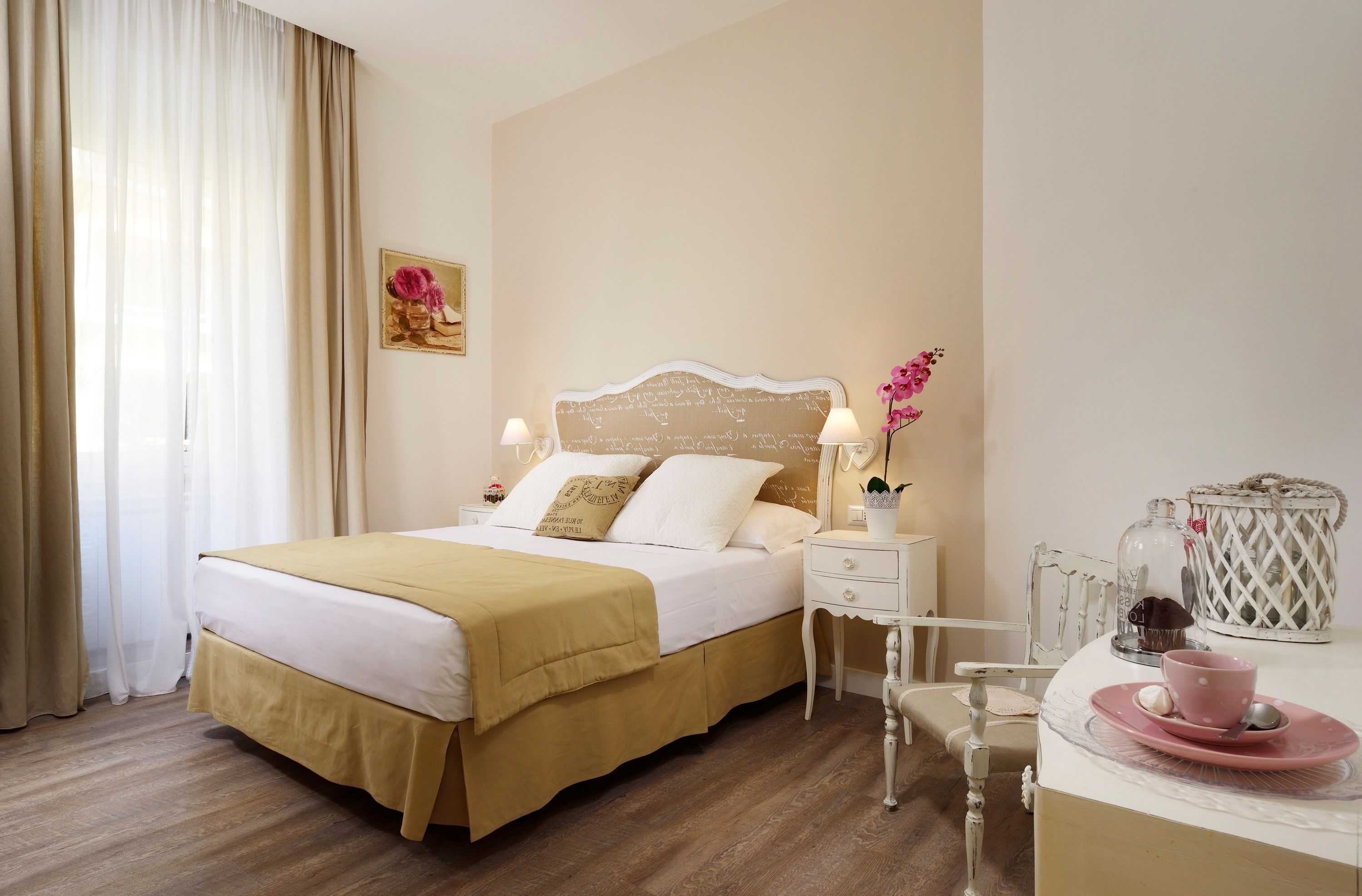 Une chambre à coucher bien rangée, avec un lit, des lampes de chevet, une petite table sur laquelle se trouvent une tasse et une soucoupe, et un vase décoratif.