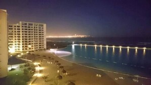 Un hotel frente a la playa con piscina, acceso directo a la arena y un horizonte urbano al fondo.