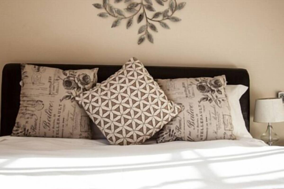 A neatly made bed with patterned pillows and a decorative wall hanging.