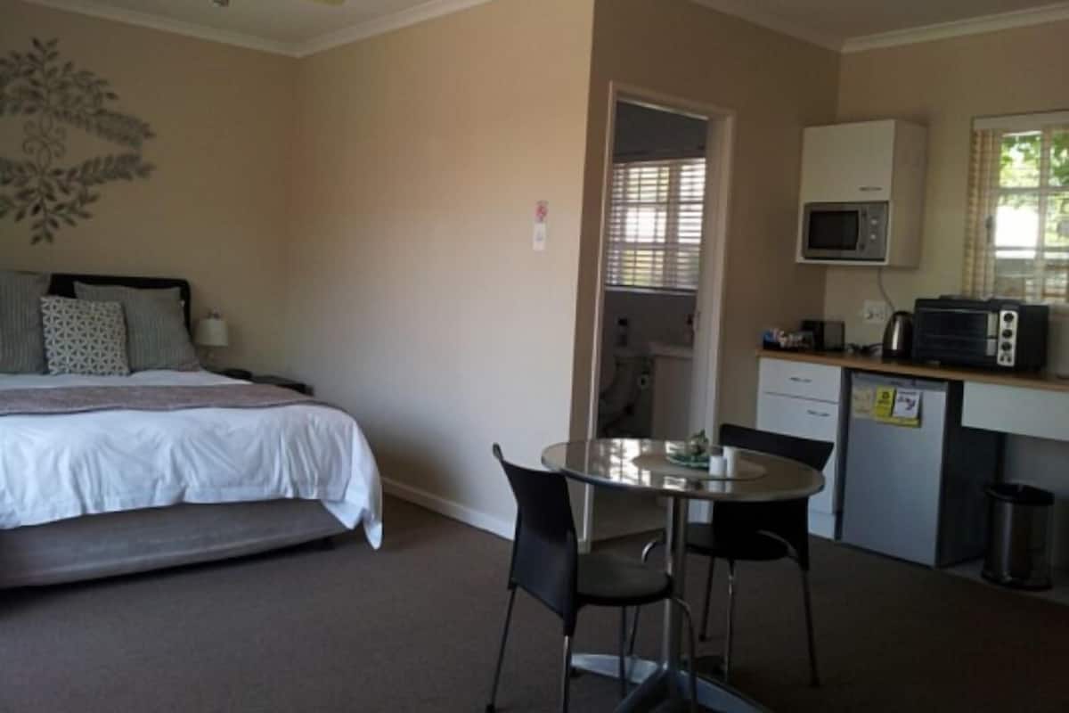 A bedroom with a bed, a desk, a microwave, and a trash can.