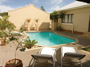 A swimming pool with lounge chairs, surrounded by potted plants and a building with a tiled roof. - Palm Beach Guesthouse (Gqeberha (Port Elizabeth))