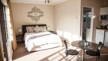 A hotel room with a bed, bedside table, lamp, and a small dining area with a table and chairs.