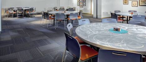 A conference room with multiple tables and chairs, carpeted flooring, and framed pictures on the walls.