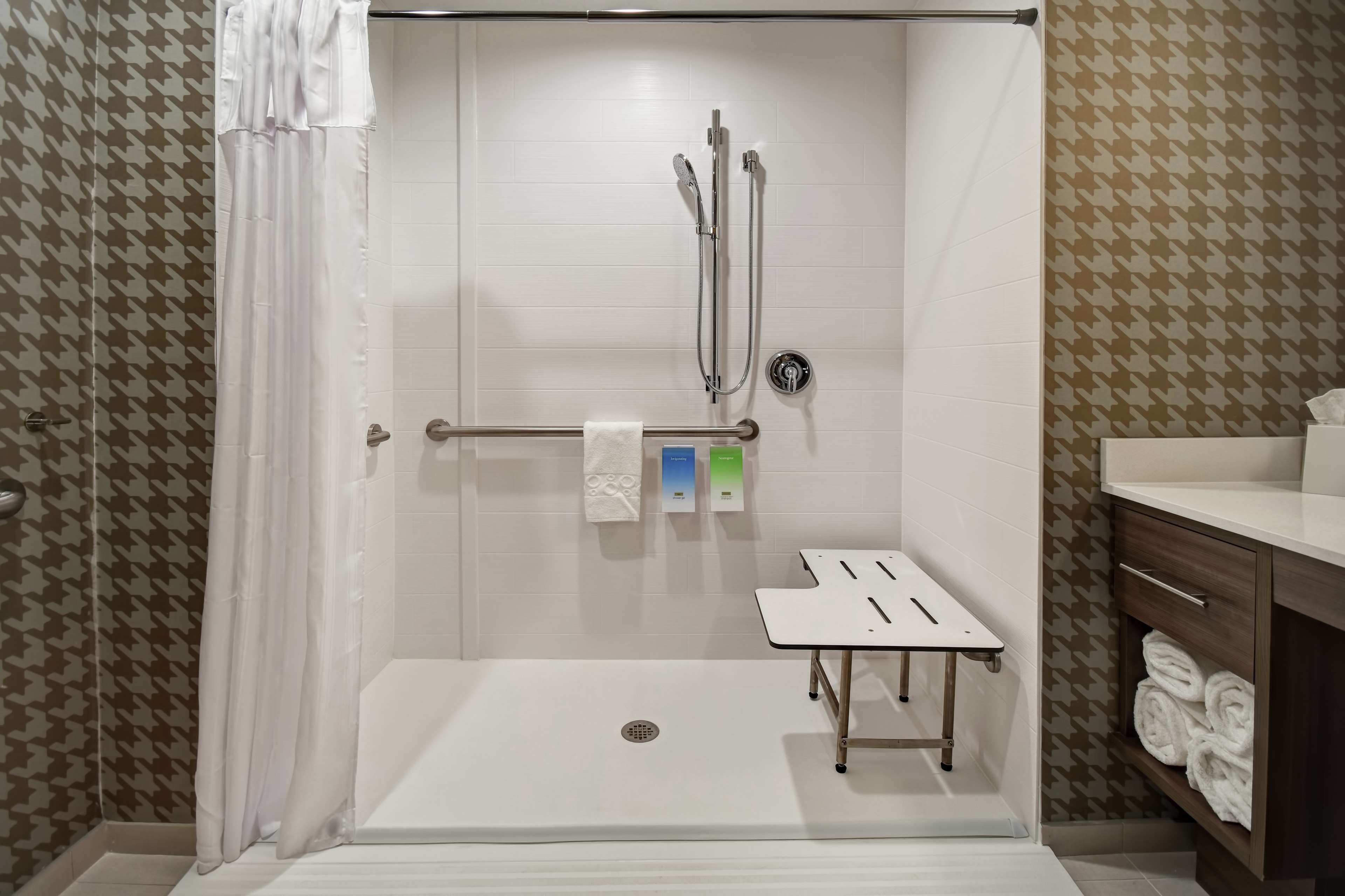 A shower area with a glass door, a towel rack with a white towel, and a small table with a pen.
