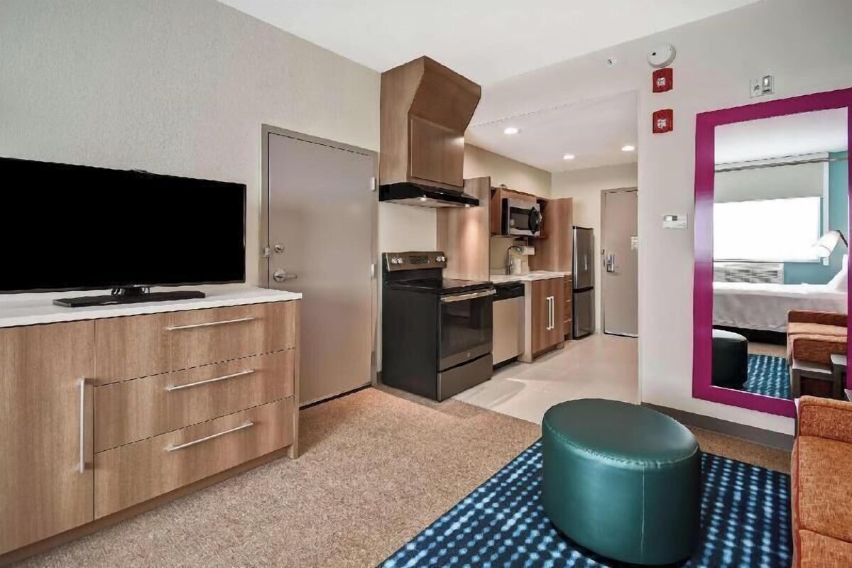 Een moderne hotelkamer met een kitchenette, een flatscreen-tv, een grote spiegel en een zithoek.