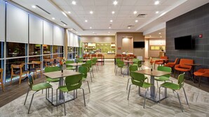 A spacious indoor dining area with multiple tables and chairs, a kitchen in the background, and a flat-screen TV mounted on the wall. - Home2 Suites by Hilton Columbus Downtown (Columbus)